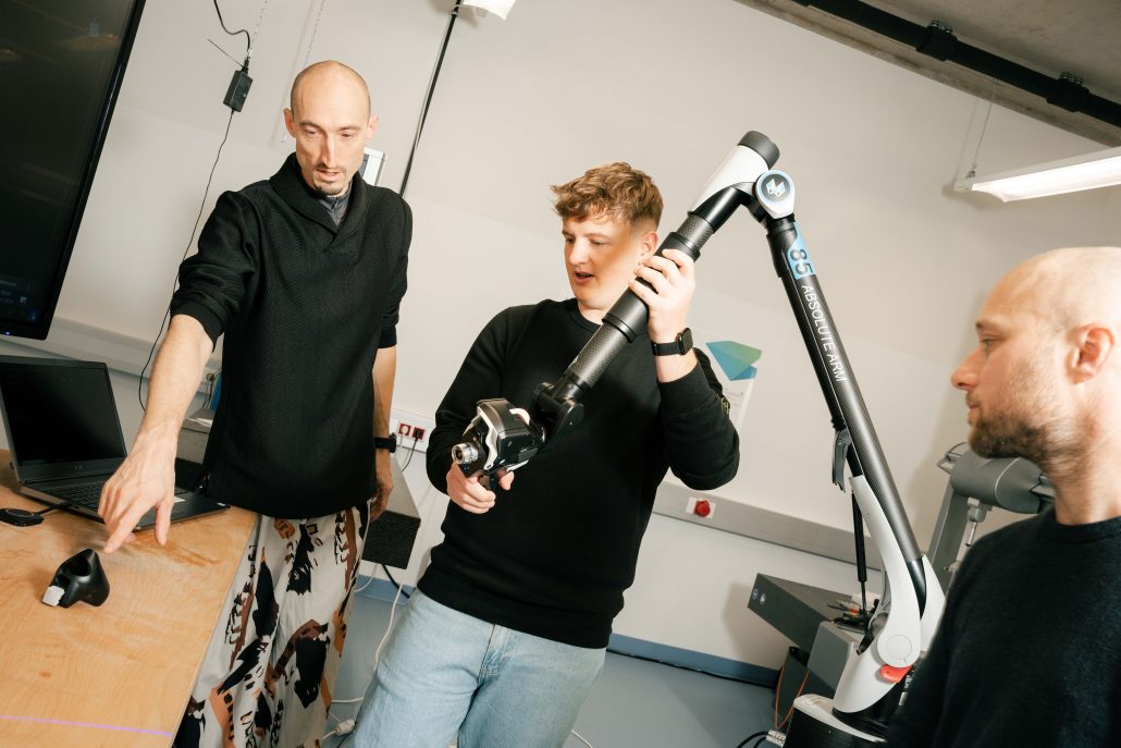 Three students examining a portable coordinate measuring arm in a university metrology lab